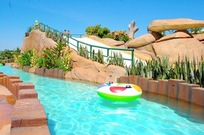 Uno scivolo acquatico con ringhiera verde, una piscina con acqua cristallina e un cerchio gonfiabile colorato.