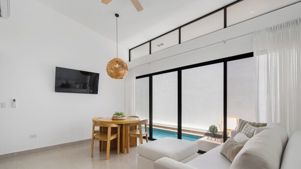 A modern living room with a sofa, dining table, and chairs. There is a large window with a view of a pool. - Sophisticated Home with a Chic Design and a Private Terrace with a Plunge Pool (Sardinal)