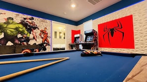 Une table de billard recouverte d’un drap bleu, entourée de murs ornés de fresques murales sur le thème des super-héros.