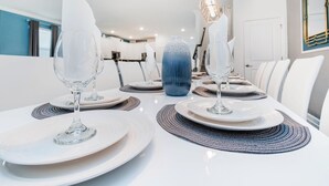 Un comedor con mesas blancas, cristalería transparente y un jarrón azul como centro de mesa.