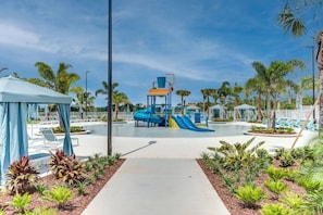 Un espace piscine doté d’une aire de jeux pour enfants, de chaises longues et de palmiers.