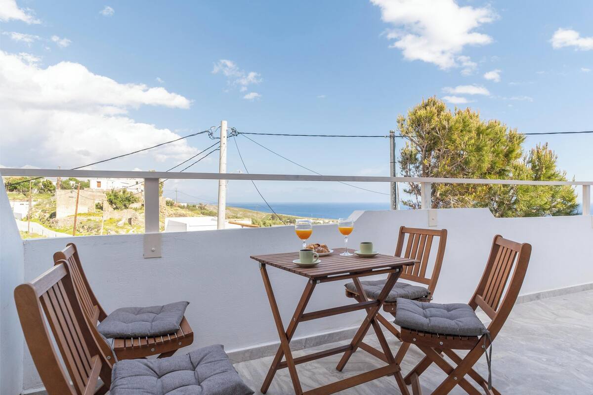 A terrace with a table and four wooden chairs, two cups of coffee and two glasses of orange juice on the table.