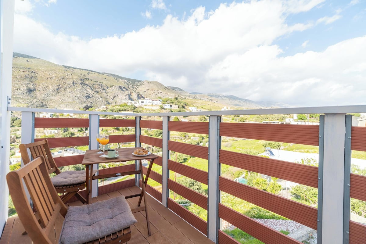 A balcony with a table, chairs, and a view of a mountainous landscape.