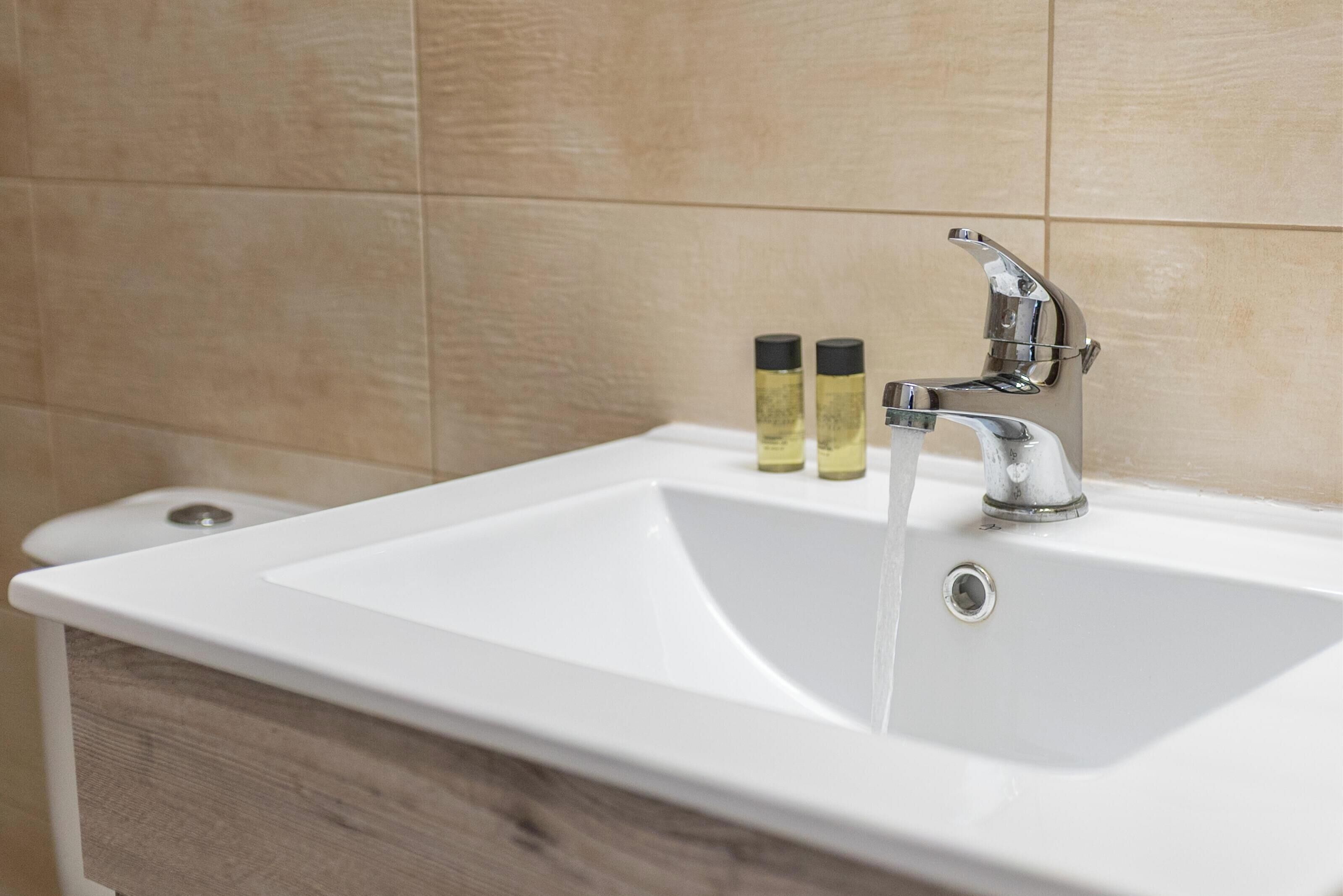 A white bathroom sink with a chrome faucet and two bottles of liquid soap.