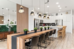 Une cuisine moderne avec un îlot central en bois, des chaises noires et des luminaires suspendus.