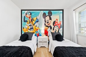 Une chambre avec deux lits, une table de chevet et une grande fresque murale sur le thème de Disney.