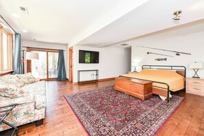 Een ruime slaapkamer met een groot bed, een sofa, een televisie en een houten kast.