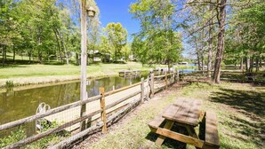 A picnic area with a wooden bench and a fence overlooking a pond.