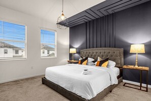 Un dormitorio con una cama grande, dos mesitas de noche, una lámpara colgante y dos ventanas.