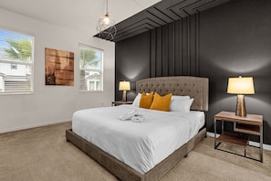 A bedroom with a large bed, two bedside tables with lamps, a geometric pendant light, and artwork on the walls.