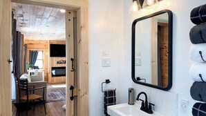 Een moderne badkamer met een wit wastafelmeubel, een zwarte kraan en een grote spiegel. Een handdoekhouder met meerdere handdoeken en een houten deur naar een andere kamer.