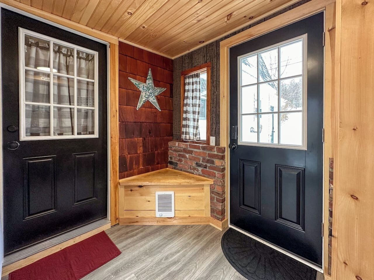 Um quarto com uma porta preta, um banco de madeira, uma decoração em forma de estrela e uma janela com cortina xadrez.