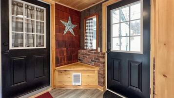 Um quarto com uma porta preta, um banco de madeira, uma decoração em forma de estrela e uma janela com cortina xadrez.