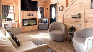 Een gezellig interieur van een blokhut met een open haard, houten wanden, een bank en een fauteuil.