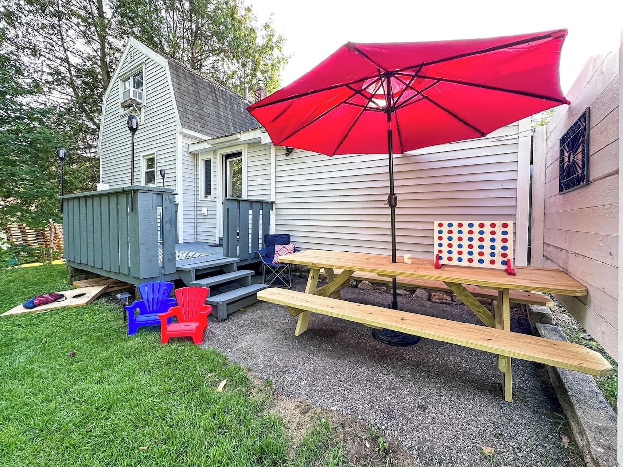 A backyard with a wooden deck, a picnic table, and a red umbrella.