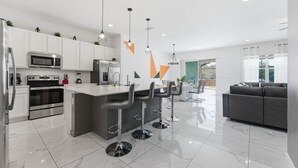 Una cocina moderna con armarios blancos, electrodomésticos de acero inoxidable y una isla central con taburetes de bar.