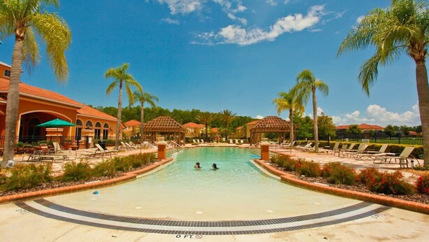 Una piscina con dos personas nadando, rodeada de palmeras y sillas de descanso.
