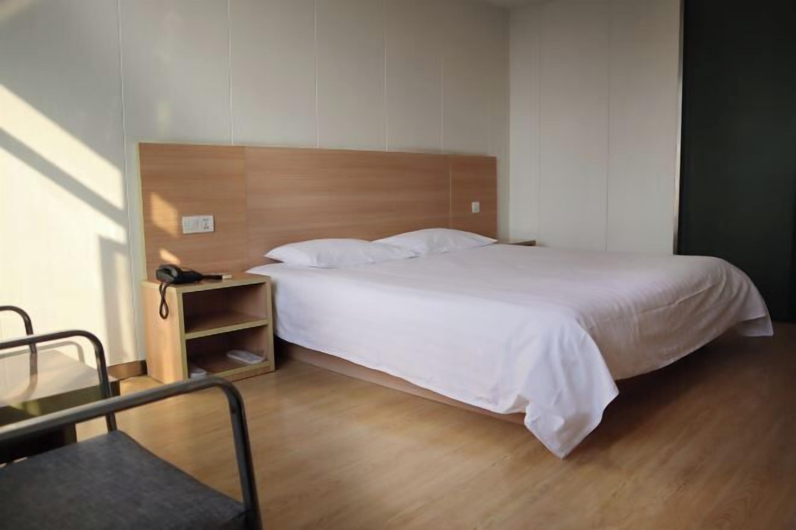 A single bed with a wooden headboard, a bedside table with a phone, and a chair.