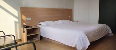 A single bed with a wooden headboard, a bedside table with a phone, and a chair.