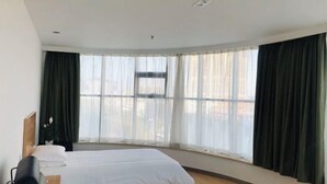 Ein Hotelzimmer mit Bett, Schreibtisch, Stuhl und einem großen Fenster mit Vorhängen.
