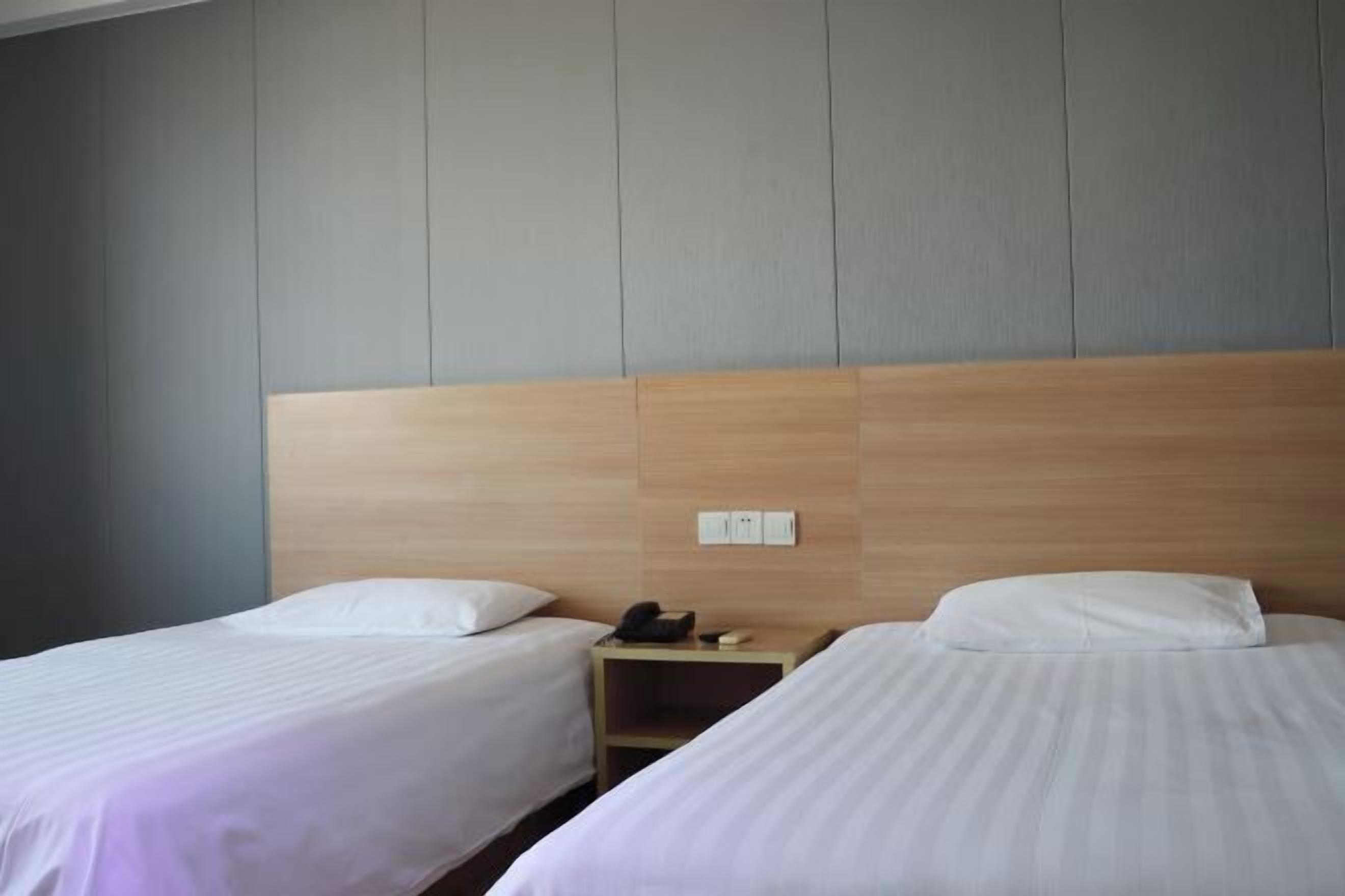 A hotel room with two single beds, a wooden headboard, a nightstand with a phone, and a wall switch.