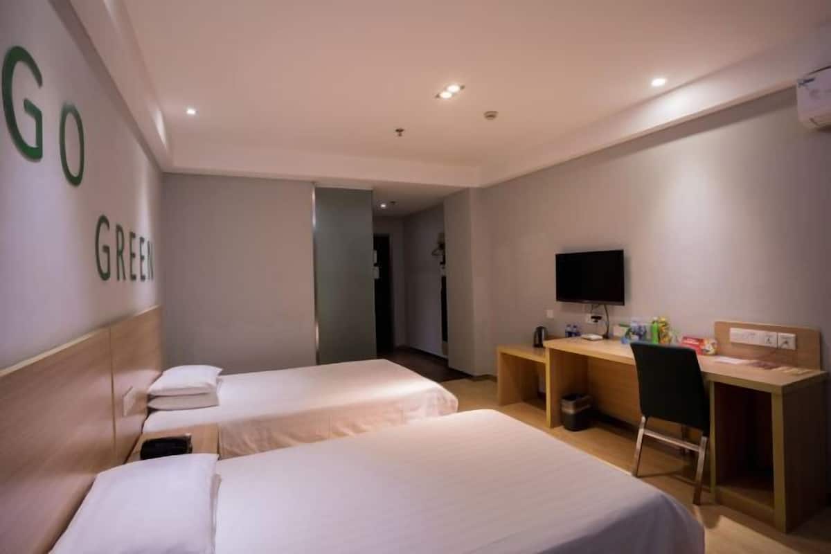 A hotel room with two beds, a desk, a chair, a television, and a wall with the word 'GREEN' visible.