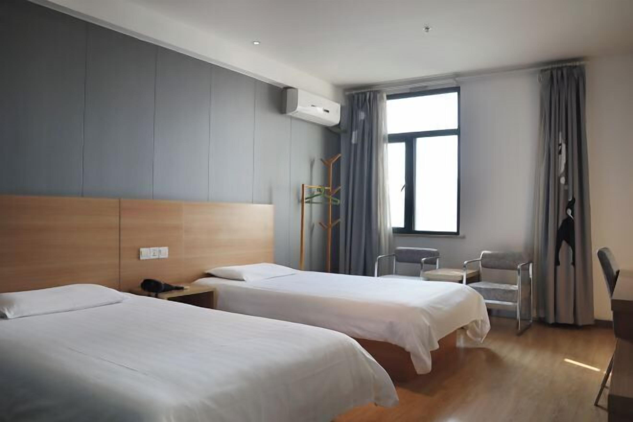 A hotel room with two beds, a desk, a chair, and a large window.