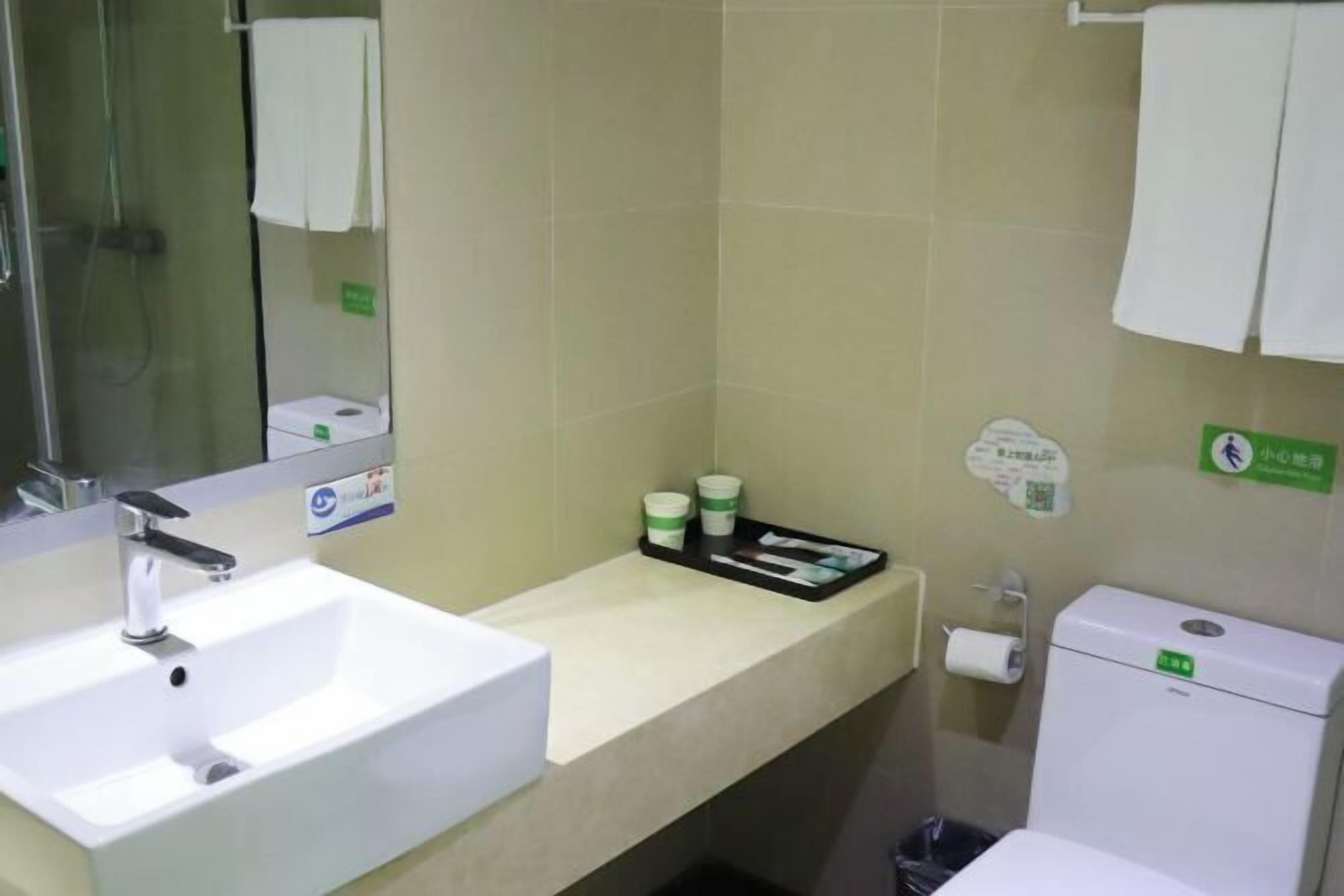 Kylpyhuone, jossa on valkoinen pesuallas, peili, wc ja hylly, jossa on hygieniatuotteita.