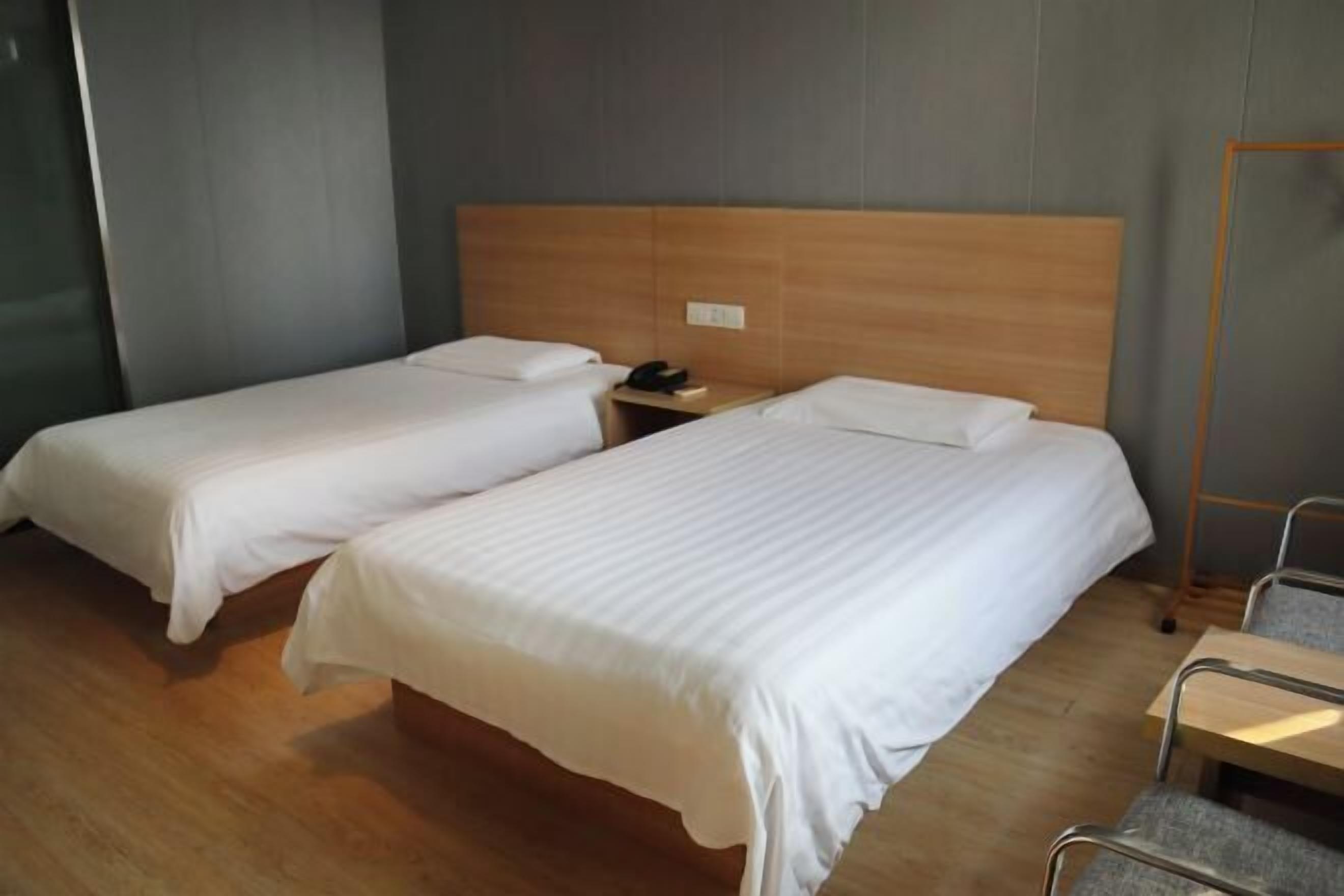 A hotel room with two single beds, a wooden headboard, a bedside table with a phone, and a chair.