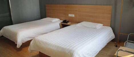 A hotel room with two single beds, a wooden headboard, a bedside table with a phone, and a chair.