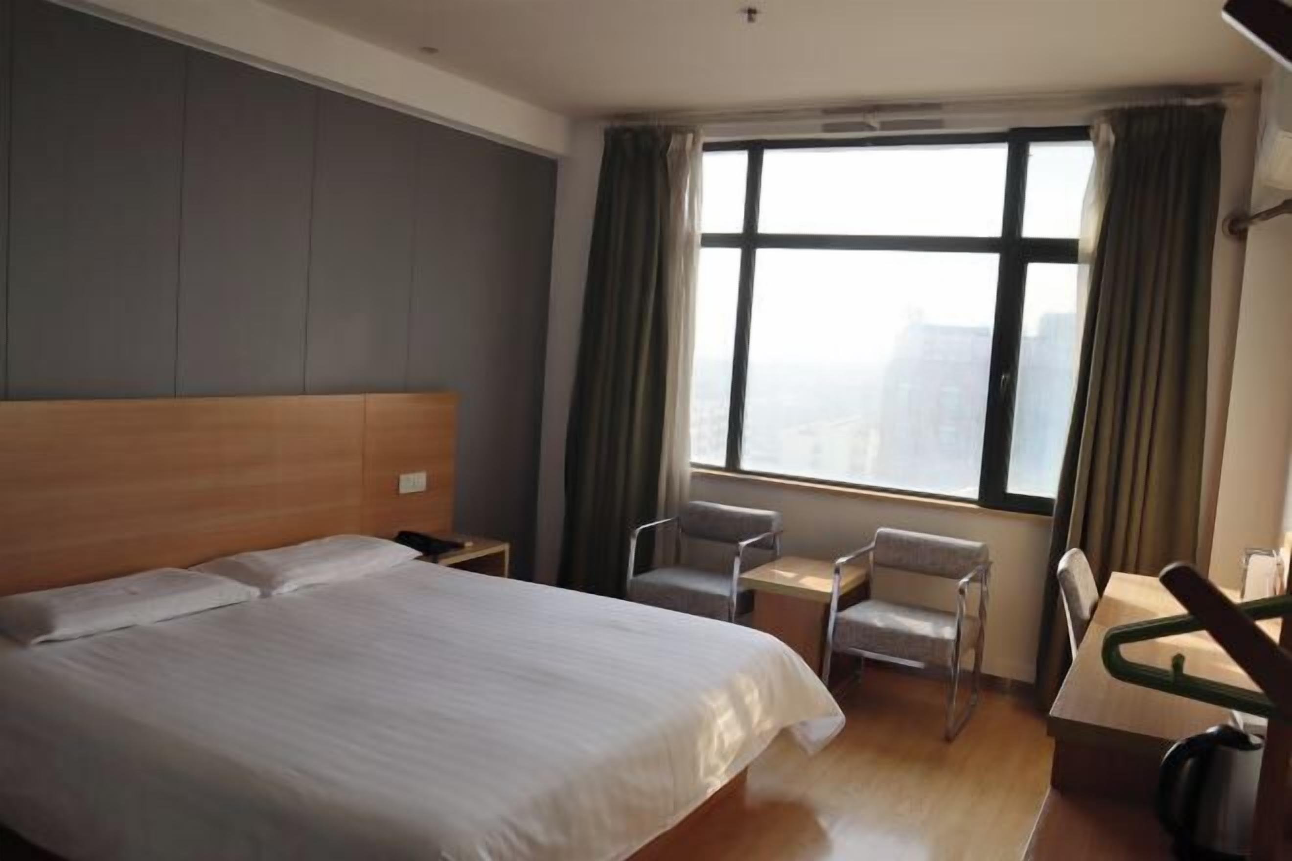 A hotel room with a large bed, a desk, two chairs, and a window with curtains.