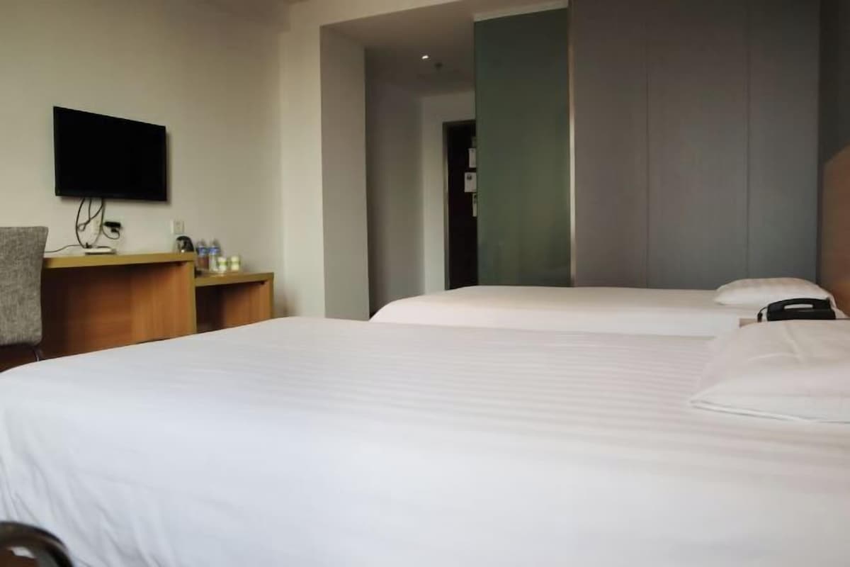 Ein Hotelzimmer mit zwei Betten, einem Schreibtisch, einem Flachbildfernseher und einem Stuhl.