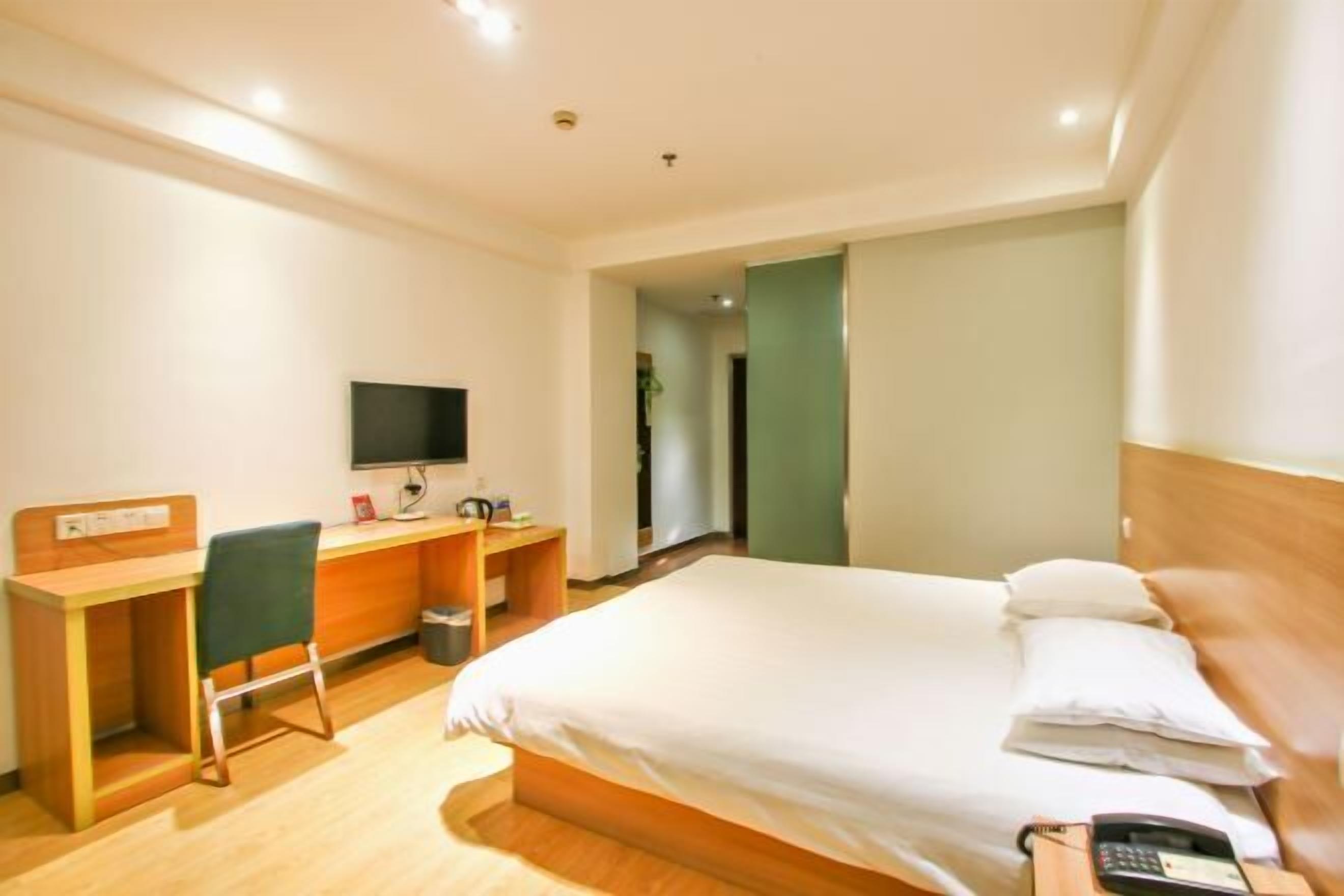 A hotel room with a bed, a desk, a chair, a television, and a telephone.