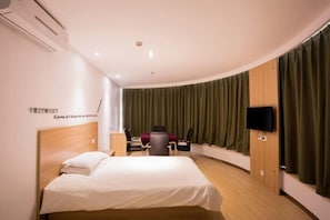 Ein Hotelzimmer mit Bett, Schreibtisch, Stuhl, Fernseher und einem Fenster mit Vorhängen.