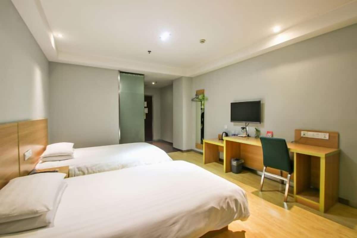 A hotel room with two beds, a desk, a chair, a TV, and a small workspace.
