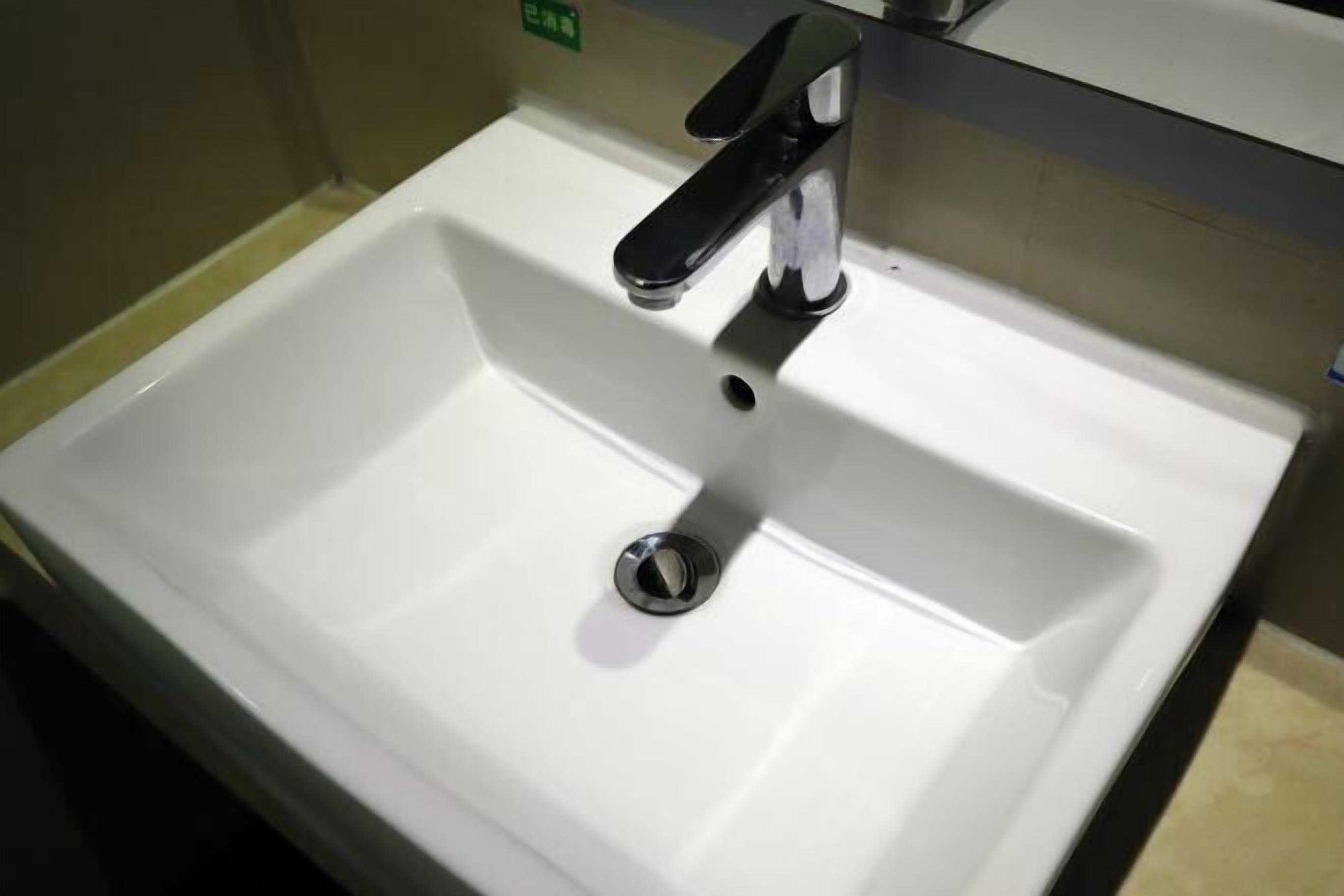 Uma pia de banheiro branca com uma torneira preta e um ralo.