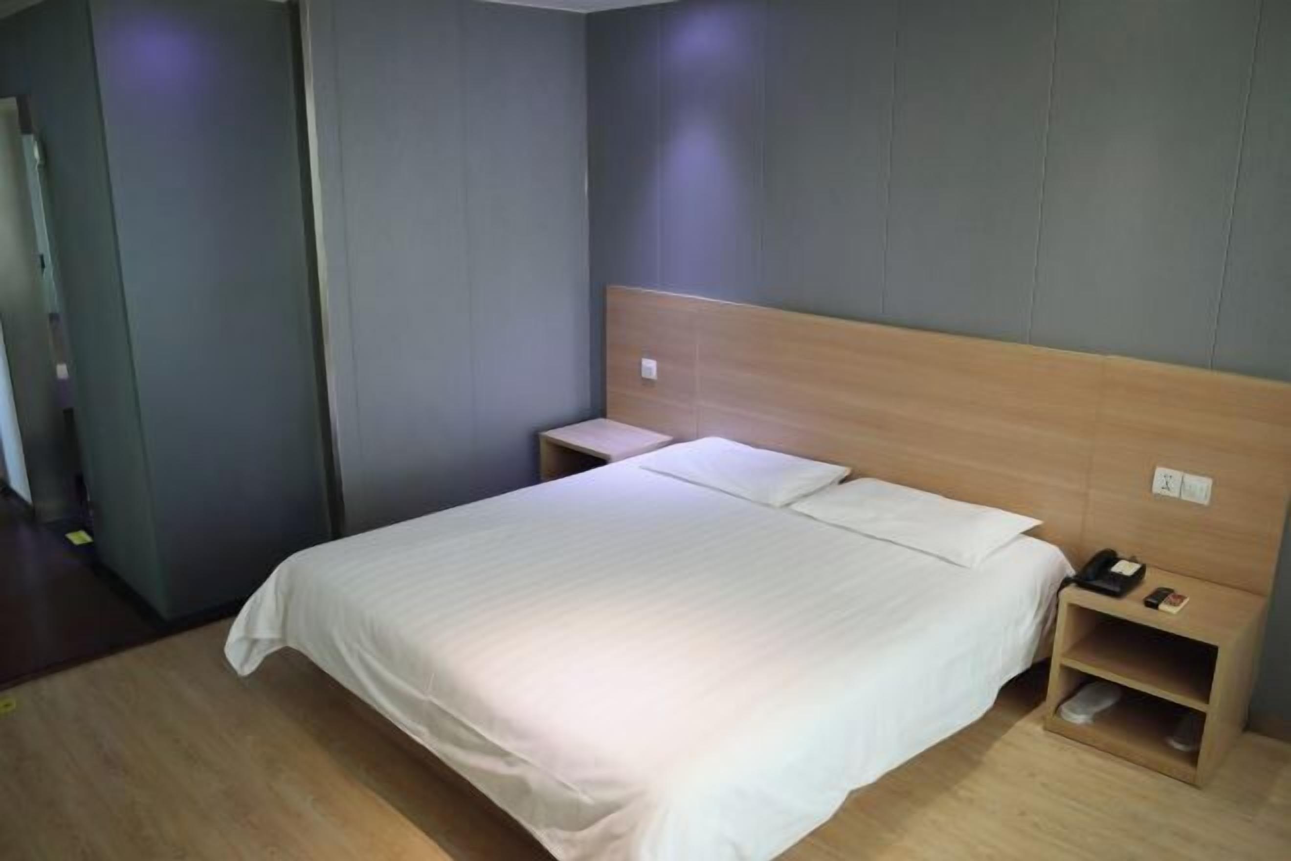 Une chambre d’hôtel avec un grand lit, une tête de lit en bois, des tables de chevet et une petite étagère.