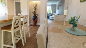Un amplio espacio de sala con una mesa de comedor, sillas, un sofá y una mesa de centro. Hay un florero con plantas secas y una vela sobre la mesa de centro.