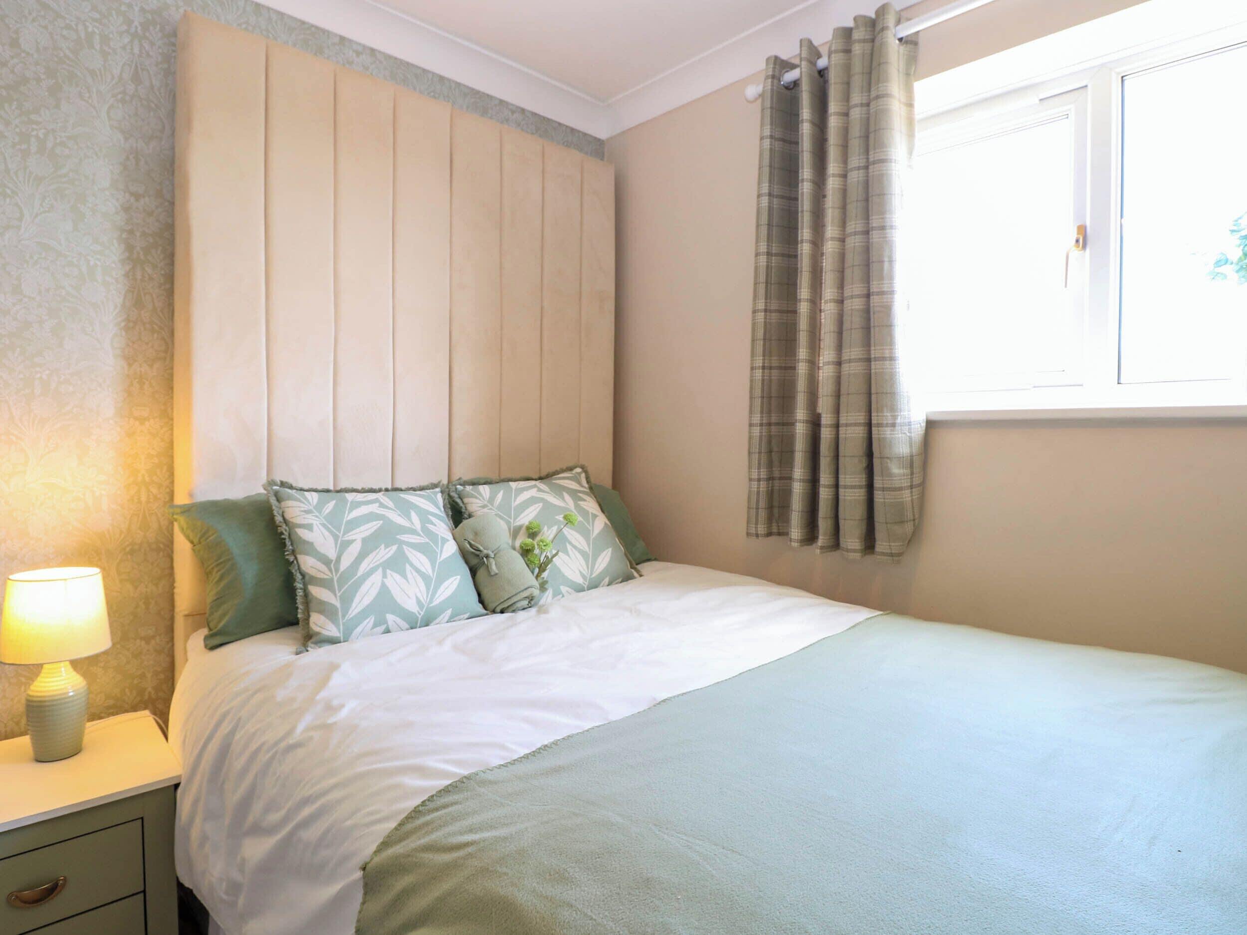 A bedroom with a bed, a nightstand with a lamp, and a window with curtains.