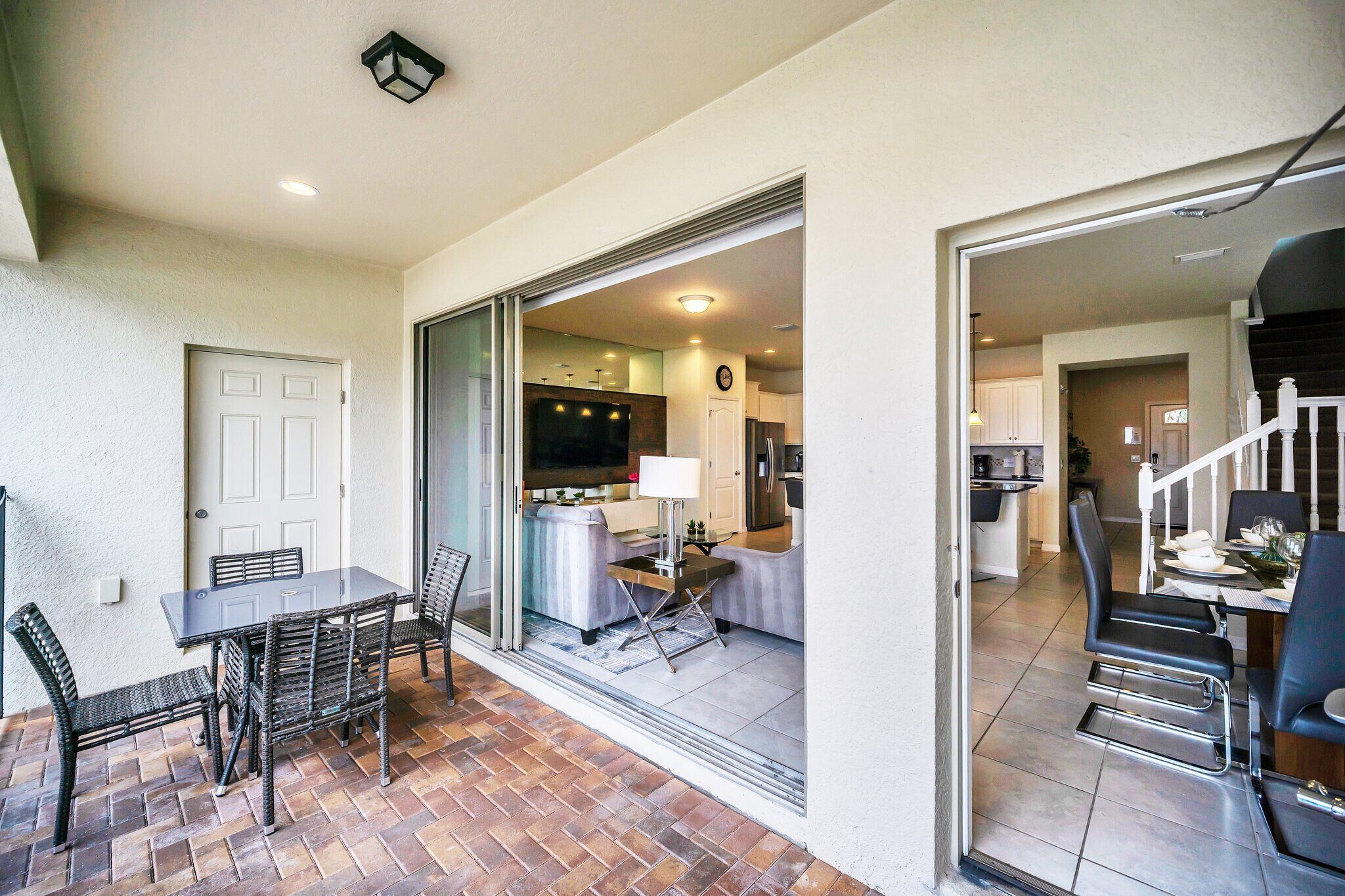 A patio with a dining table and chairs, a kitchen in the background, and a staircase leading to another level.