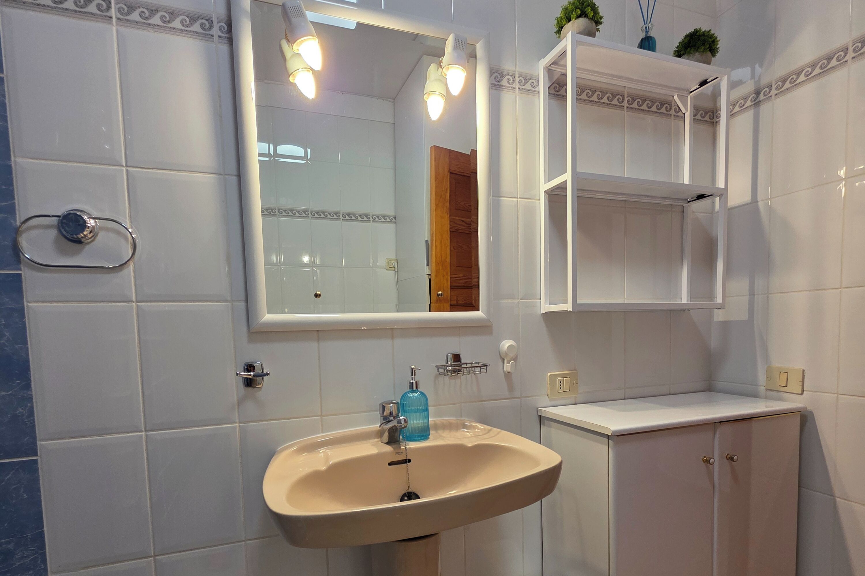 Un baño con un lavamanos color crema, azulejos blancos, un espejo y una puerta de madera.