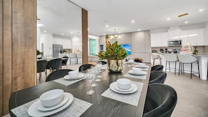 A modern dining area with a long table set for six, a kitchen in the background, and a large plant centerpiece. - Last Minute Disney! Private Pool, Hot Tub & Themed Bedrooms. Book Now! #124375 (Orlando)