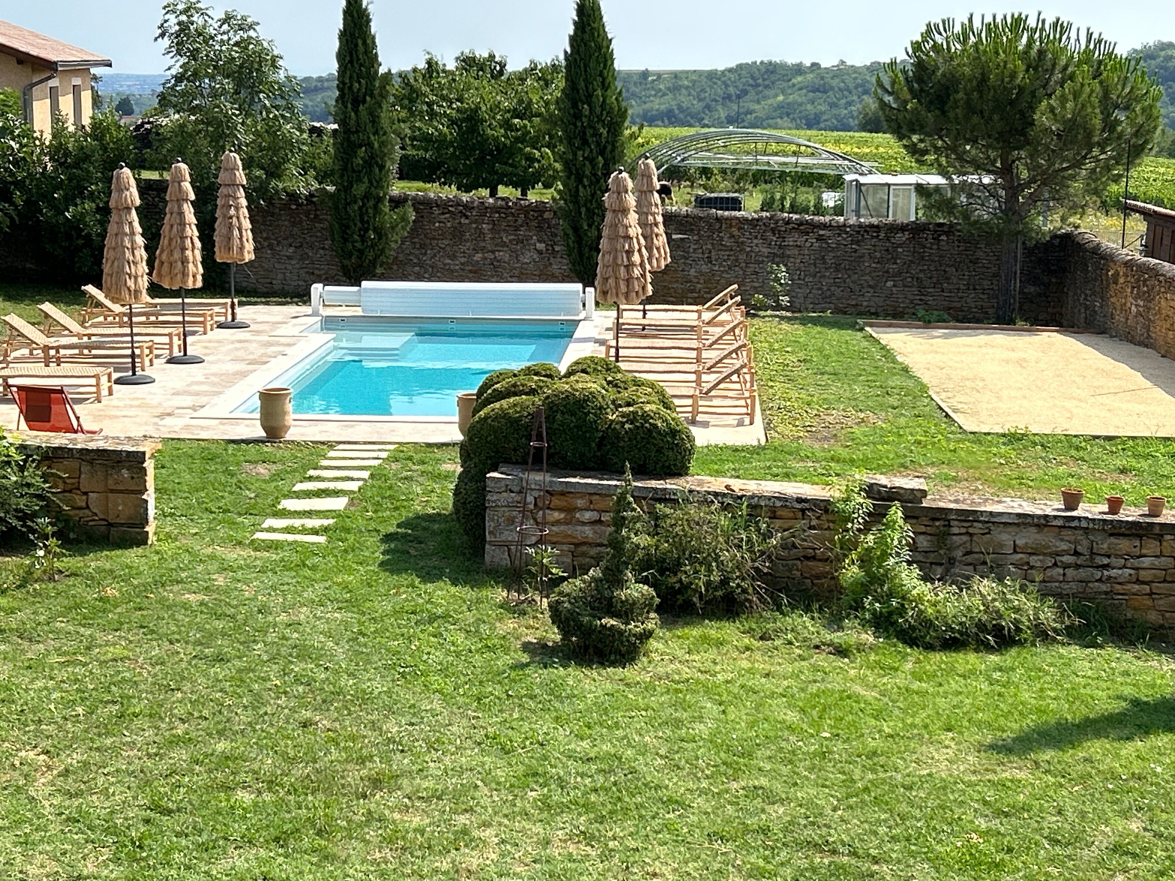 A swimming pool with lounge chairs and umbrellas, surrounded by stone walls and greenery.