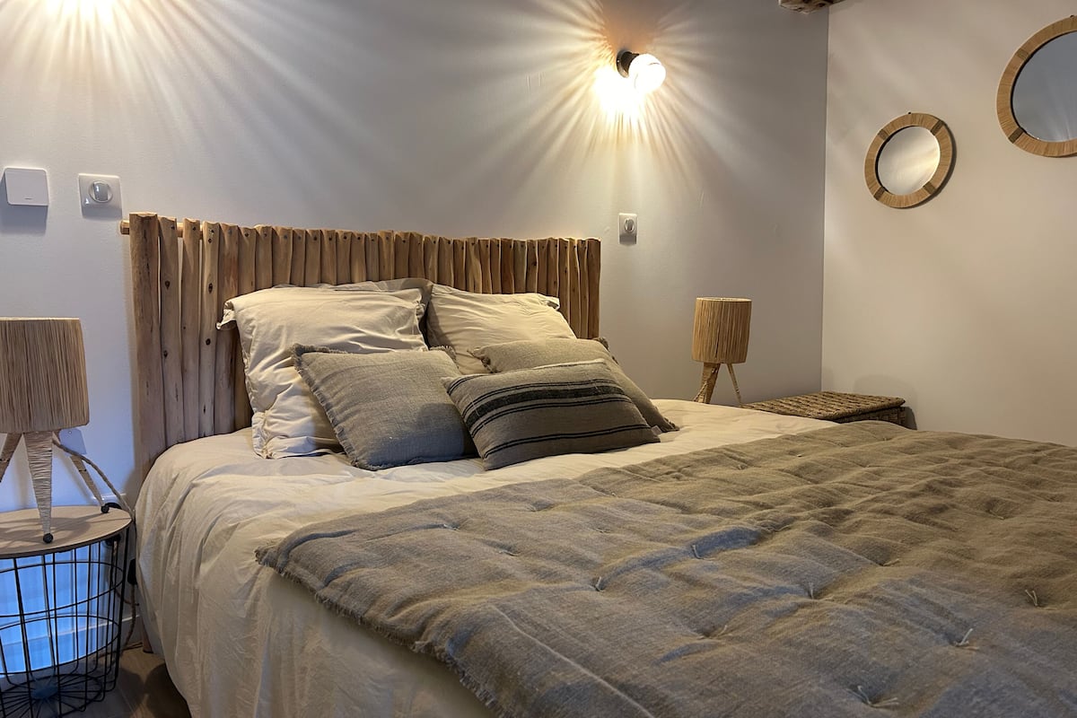 Un lit bien fait, avec une couverture à motifs, une tête de lit en bois et deux lampes fixées au mur.
