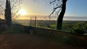 Eine Steinmauer mit Schaukel und Grillplatz mit Blick auf eine ländliche Landschaft bei Sonnenuntergang.