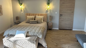 Ein Schlafzimmer mit Bett, Nachttischen, einer Bank, einer Tür und Holzbalken an der Decke.