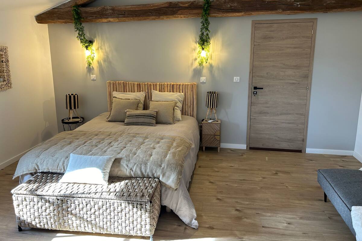 Une chambre à coucher avec un lit, des tables de chevet, un banc, une porte et des poutres en bois au plafond.