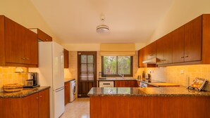A modern kitchen with wooden cabinets, granite countertops, a built-in oven, and a window with blinds. - Villa Pleiades - sea views, private pool & hot tub (Kouklia)