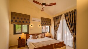 A bedroom with a wooden bed, two bedside tables with lamps, a ceiling fan, and large windows with curtains. - Villa Pleiades - sea views, private pool & hot tub (Kouklia)