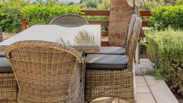 An outdoor patio with wicker furniture, a table, and chairs, under a palm tree with an umbrella. - Villa Pleiades - sea views, private pool & hot tub (Kouklia)